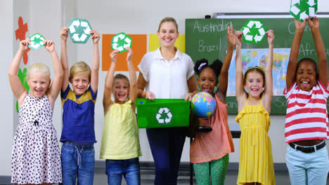 School-kids-and-teacher-holding-recycling-symbols-and-globe-in-classroom