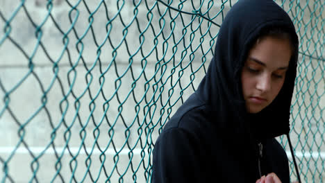 Sad-schoolgirl-in-hooded-leaning-against-fence