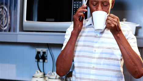 Älterer-Mann-Telefoniert-Mit-Dem-Handy,-Während-Er-In-Der-Küche-Kaffee-Trinkt