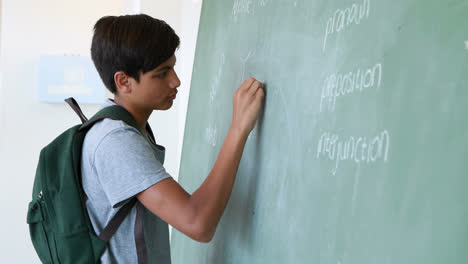 Schoolboy-writing-on-green-chalkboard-in-classroom