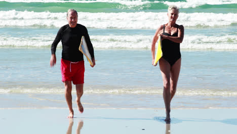 Senior-couple-with-surfboard-running-on-beach