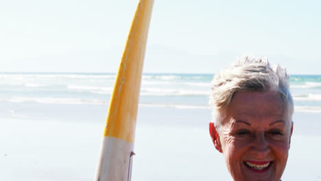 Senior-woman-with-surfboard-standing-on-beach