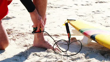 Senior-man-tying-surfboard-leash-to-ankle