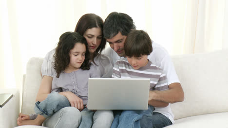 Familia-Sonriente-En-Casa-Usando-Una-Computadora-Portátil