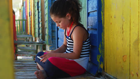 Chica-Usando-Tableta-Digital-Cerca-De-Una-Colorida-Cabaña-En-La-Playa