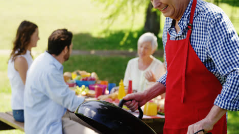 Senior-man-preparing-food-on-barbecue-in-the-park