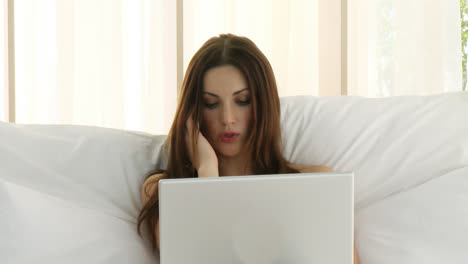 Close-up-of-a-woman-using-a-laptop-and-talking-on-phone-in-bed