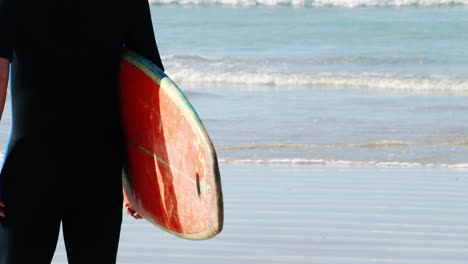 Senior-man-with-surfboard-standing-on-beach