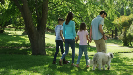 Family-walking-with-their-dog-in-the-park-on-a-sunny-day