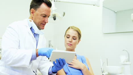 Dentist-discussing-over-digital-tablet-with-female-patient