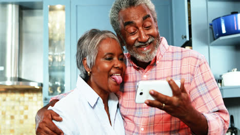 Senior-couple-taking-selfie-from-mobile-phone-in-kitchen
