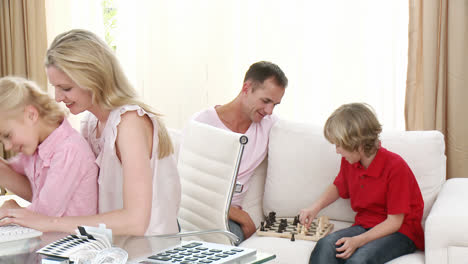 Mother-and-daughter-using-a-computer-and-father-and-son-playing-chess