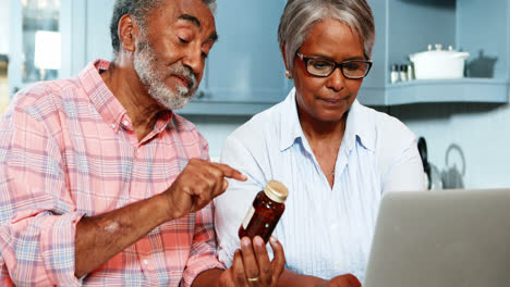 Älteres-Paar-Hält-Medizinflasche-Und-Benutzt-Laptop
