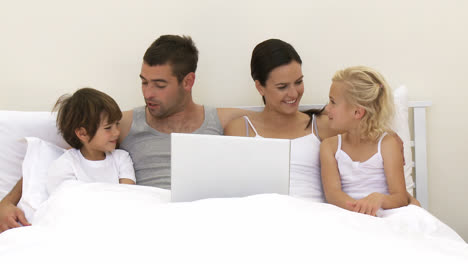 Familia-Usando-Una-Computadora-Portátil-En-La-Cama