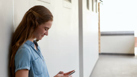 Happy-schoolgirl-using-mobile-phone-in-corridor