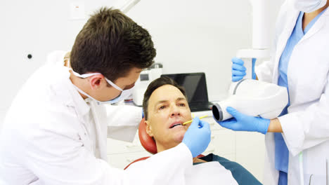 Dentist-examining-a-male-patient-with-tool