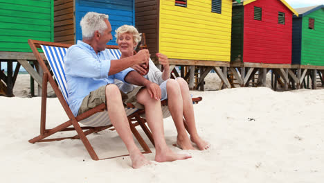 Senior-couple-toasting-drinks-near-colorful-beach-hut