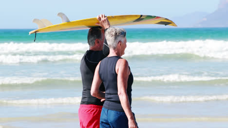 Senior-couple-carrying-surfboard-over-head-while-walking-on-beach