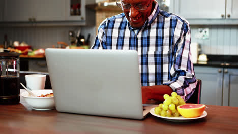 Smiling-senior-man-using-laptop-while-having-breakfast