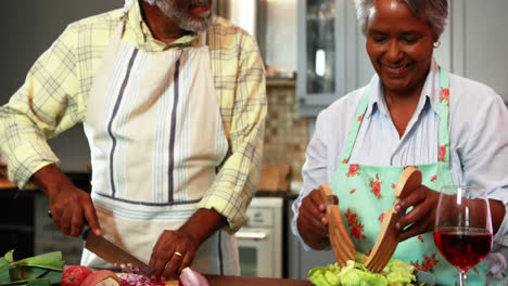 Senior-man-chopping-vegetables-while-woman-preparing-salad-in-kitchen