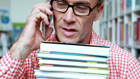 Male-teacher-talking-on-mobile-phone-in-library