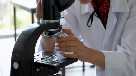 Schoolgirl-experimenting-on-microscope-in-laboratory