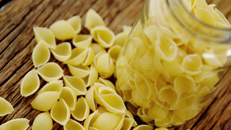 Scattered-conchiglion-pasta-on-wooden-background-and-tidied-in-glass-jar