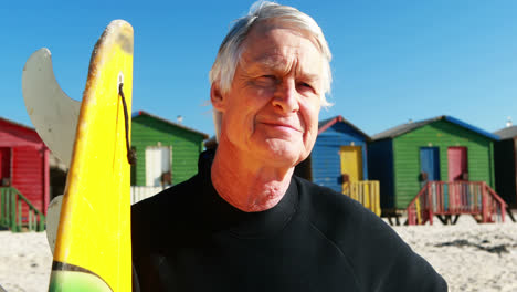 Senior-man-with-surfboard-standing-on-beach