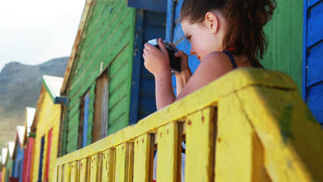 Chica-Fotografiando-Con-Cámara-Desde-Una-Colorida-Cabaña-En-La-Playa.