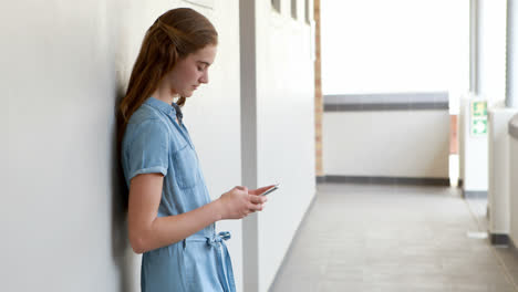Happy-schoolgirl-using-mobile-phone-in-corridor