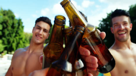 Group-of-male-friends-toasting-beer-bottles-at-poolside