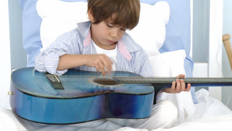Close-up-of-little-boy-playing-guitar-on-bed