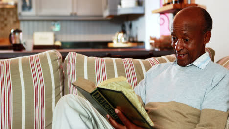 Senior-man-reading-book-in-living-room