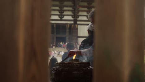 Mann-Mit-Gesichtsmaske-Steht-Neben-Räuchergefäß,-Um-Räucherstäbchen-Mit-Der-Großen-Buddha-Halle-Des-Todaiji-Tempels-Im-Hintergrund-In-Nara,-Japan-Anzuzünden