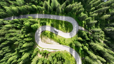 Camper-van-driving-on-snake-road-in-forestry-mountains,-top-down-view
