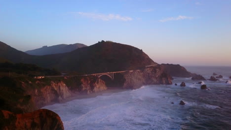 Bixby-Creek-Bridge-Big-Sur-California-aerial-cinematic-drone-flight-Pacific-Ocean-Nor-Cal-winter-summer-big-wave-swell-crashing-shoreline-late-afternoon-golden-hour-sunset-upward-slowly-movement