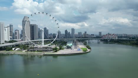 Toma-De-Drones-Del-Paseo-Marítimo-Y-El-Ojo-Del-Volante-De-Singapur,-Cámara-Orbitando-Alrededor-De-La-Pista-Marina-Bay-F1