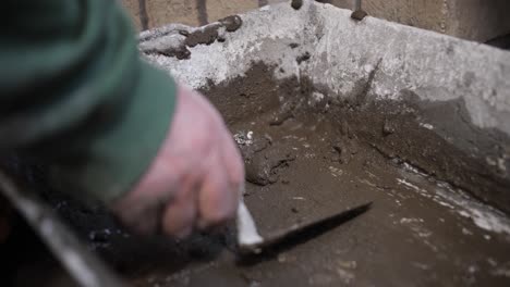 Primer-Plano-De-Una-Mano-Mezclando-Hormigón-Húmedo-Con-Una-Paleta-En-Un-Balde-En-Un-Sitio-De-Construcción