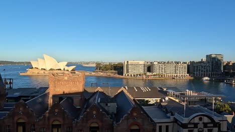 Slow-pan-left-view-looking-over-rooftops-towards-Circular-Quay,-Sydney-with-the-Opera-House-in-sunlight