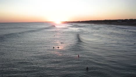 Surfers-catch-the-last-waves-at-sunset,-golden-hues-on-the-ocean,-serene-atmosphere