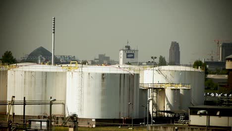 Industrial-fuel-storage-tanks-with-city-skyline-in-the-background,-conveying-a-sense-of-energy-and-urban-industry