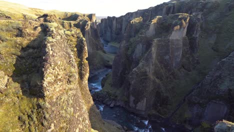 A-majestic-river-cutting-through-a-green-canyon-in-iceland,-sunlight-casting-shadows-,-aerial-view