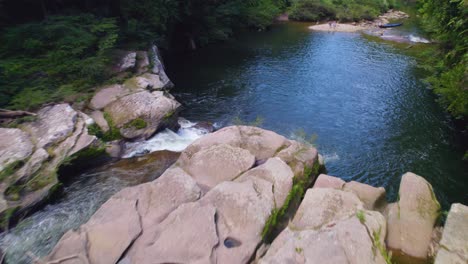 Ruhiger-Fluss-Mit-Moosbedeckten-Felsen-In-Oxapampa,-Peru,-Mit-üppigem-Wald-Im-Hintergrund,-Tageslicht,-Luftaufnahme