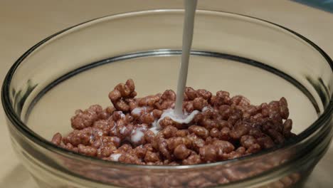 Milk-pouring-into-chocolate-cereal-in-a-clear-bowl,-breakfast-close-up-shot