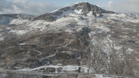 Aerial-shot-over-the-Old-Man-of-Storr-on-Skye,-winding-trails-visible-amidst-snow-dusted-rocky-landscape,-winter