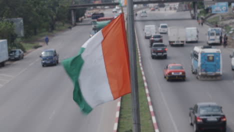 Nahaufnahme-Der-Ivorischen-Flagge,-Die-Auf-Einer-Stange-In-Der-Mitte-Der-Autobahn-Weht