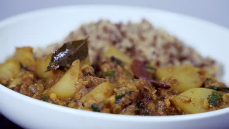 Visual-appealing-food-shot-of-papaya-curry-rotating-on-a-platter-inside-a-white-dish-with-quinoa-and-chili-pepper-visible-and-bay-leaves