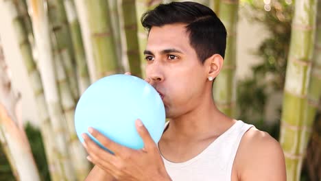 Portrait-of-young-latin-man-inflating-a-latex-balloon