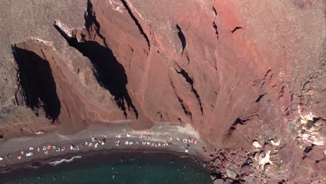 Aerial-Bird-Eye-View-over-Red-Beach-full-of-Tourists-and-Bathers,-Santorini