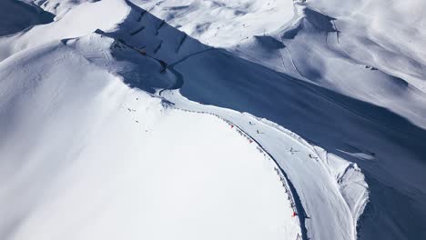 several-skiers-ski-down-a-slope-in-snow-covered-mountains